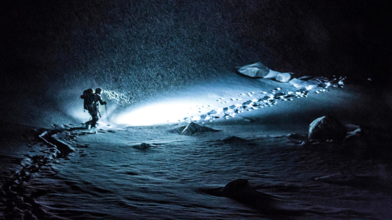 un randonneur la nuit dans la neige avec une lampe frontale en lupine